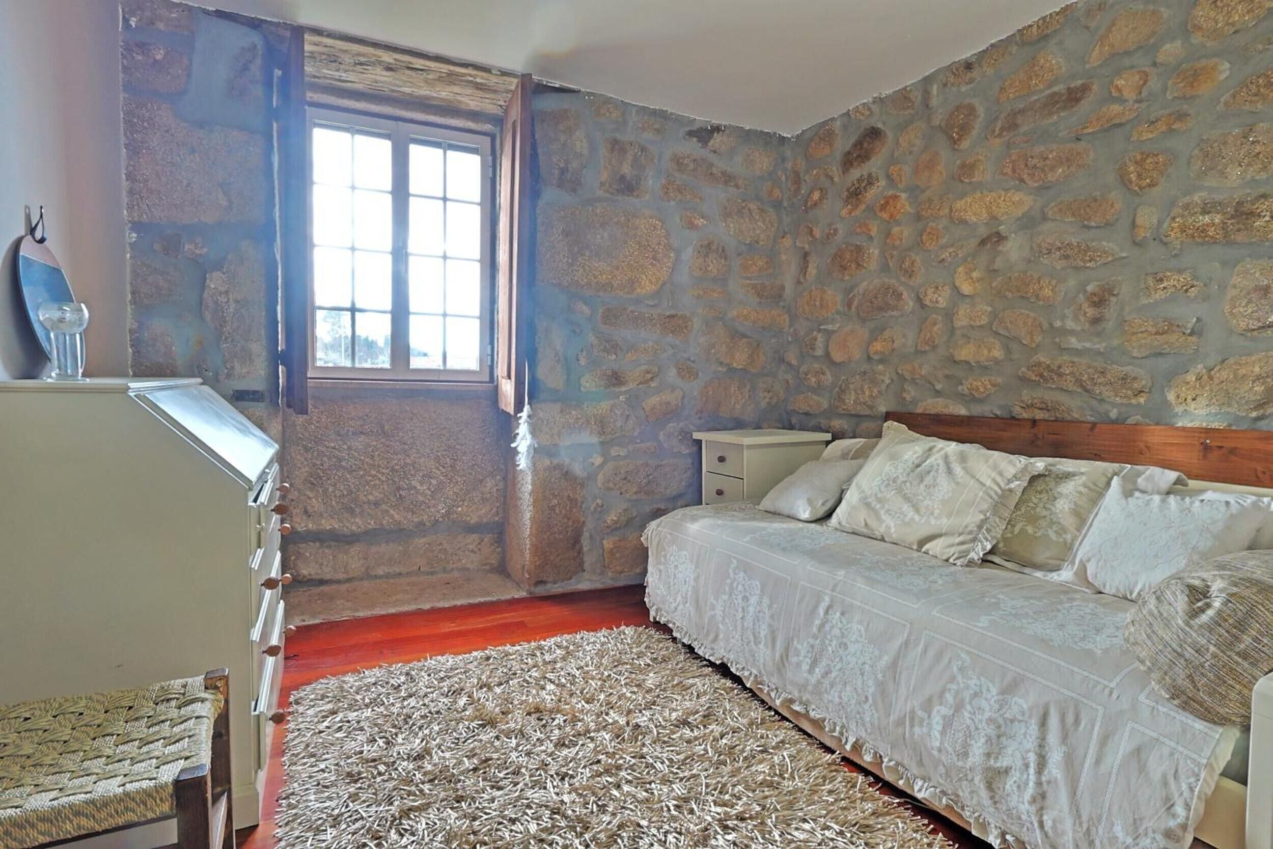 Ein Schlafzimmer mit Steinwand, einem Holzbett, einem Fenster und einem kleinen Nachttisch.