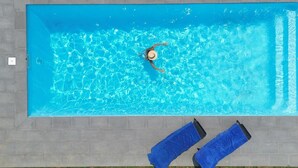 Une piscine rectangulaire à l’eau d’un bleu limpide, entourée d’une terrasse carrelée de couleur grise.