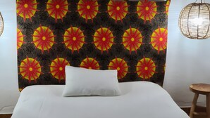 A bed with a white comforter, a headboard with a floral tapestry, and a small wooden stool.