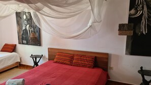 A bedroom with a wooden headboard, a red bedspread, two pillows, a small table, and a chair.