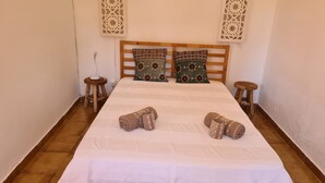 A neatly made bed with patterned pillows, two small stools, and a decorative wall piece. - Cottage 'Casa 4' with Shared Pool, Private Terrace and Wi-Fi (Ribeira da Azenha)