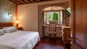 A bedroom with a bed, a desk, a chair, a window with a view of greenery, and a wooden ceiling. - Room 'Carbayu' with Mountain View, Shared Garden and Wi-Fi (Con)