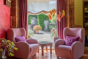 A room with two armchairs, a small table, a view of a garden with stone structures, and a bookshelf. - Inn 'Arciu' with Mountain View, Shared Garden and Wi-Fi (Con)