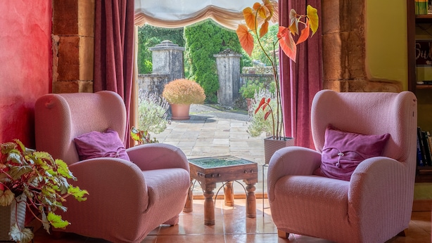 A room with two armchairs, a small table, a view of a garden with stone structures, and a bookshelf. - Room 'Araucaria' with Mountain View, Shared Garden and Wi-Fi (Con)