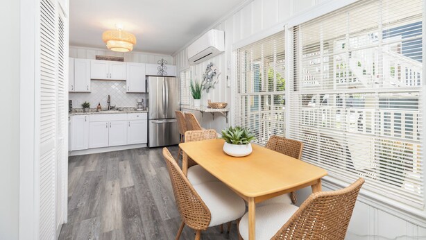 Une cuisine moderne avec des meubles blancs, un réfrigérateur en acier inoxydable et un coin repas comprenant une table en bois et des chaises en osier.