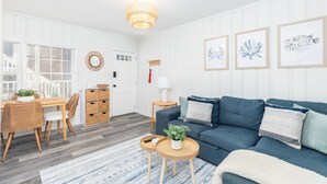 Un salon moderne avec un canapé bleu, des meubles en osier et des œuvres d’art encadrées accrochées au mur.