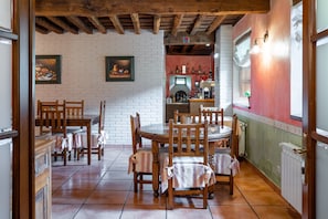 Un espace repas avec des tables et des chaises en bois, un mur de briques orné de tableaux encadrés, et un coin cuisine avec un mur rouge et des armoires blanches.