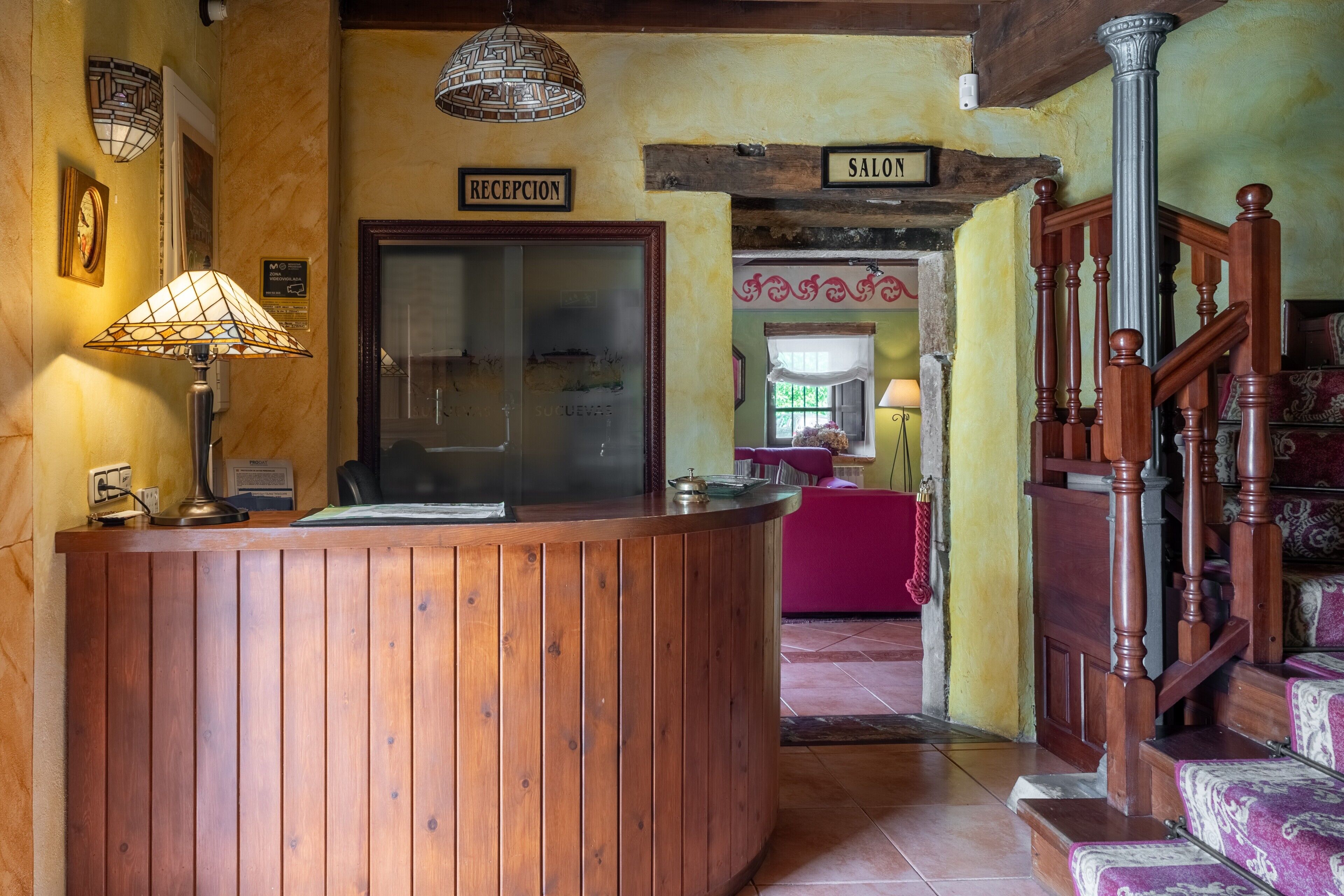A reception desk with a wooden finish, a reception sign, a staircase with a wooden railing, and a sign indicating the direction to the salon.