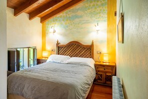 A bedroom with a wooden headboard, two bedside lamps, a bed with white linens, a wooden nightstand, and a wall with a leaf pattern. - Room 'Castañu' with Mountain View, Shared Garden and Wi-Fi (Con)