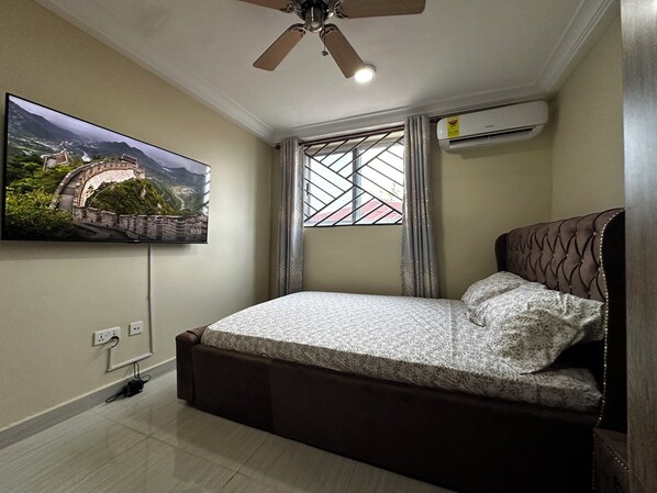 Un dormitorio con cama, ventilador de techo, televisor montado en la pared y aire acondicionado.