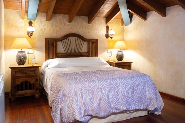 A bedroom with a wooden headboard, two bedside tables with lamps, a patterned bedspread, and a stone-patterned wall.