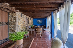 A covered outdoor seating area with stone walls, wooden furniture, and potted plants.