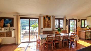 Un comedor con mesa y sillas, una cocina con pileta y muebles, y una vista a través de puertas de vidrio.