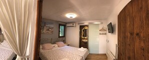 Un dormitori amb un llit, una finestra, un aparell d'aire condicionat, un mirall i una porta de fusta.