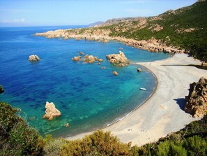 Un paisaje costero con aguas azules cristalinas, afloramientos rocosos y una playa arenosa.