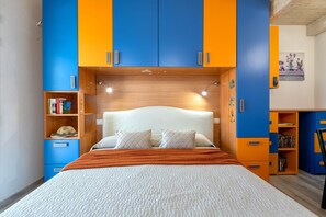 A bedroom with a bed, a nightstand, a bookshelf, and a desk with a chair.