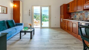 Una cocina moderna con armarios de madera, una zona de comedor con un sofá azul y un amplio ventanal corredera que da a un balcón.