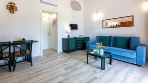 Un salón con un sofá azul, un mueble verde, una mesita con un jarrón y un televisor fijado a la pared.