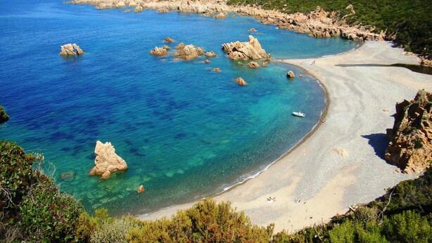 Un paisaje costero con aguas azules cristalinas, afloramientos rocosos y una playa arenosa.