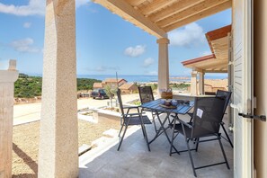 A covered patio with a table and chairs, overlooking a residential area and the sea.