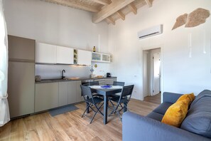 A modern kitchen with a dining table, chairs, and a grey sofa with a yellow pillow.