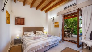 Een slaapkamer met een bed, nachtlampen, een houten plafond, een airconditioning en een raam met gordijnen, plus een uitzicht op een buitengebied.