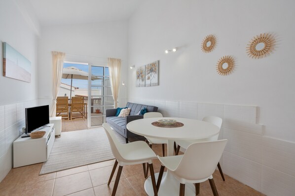 A modern living room with a TV, dining table, and chairs, a sofa, and a balcony with a view.