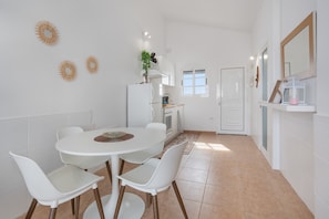 A compact kitchen with white appliances, a dining table with chairs, and a small island.