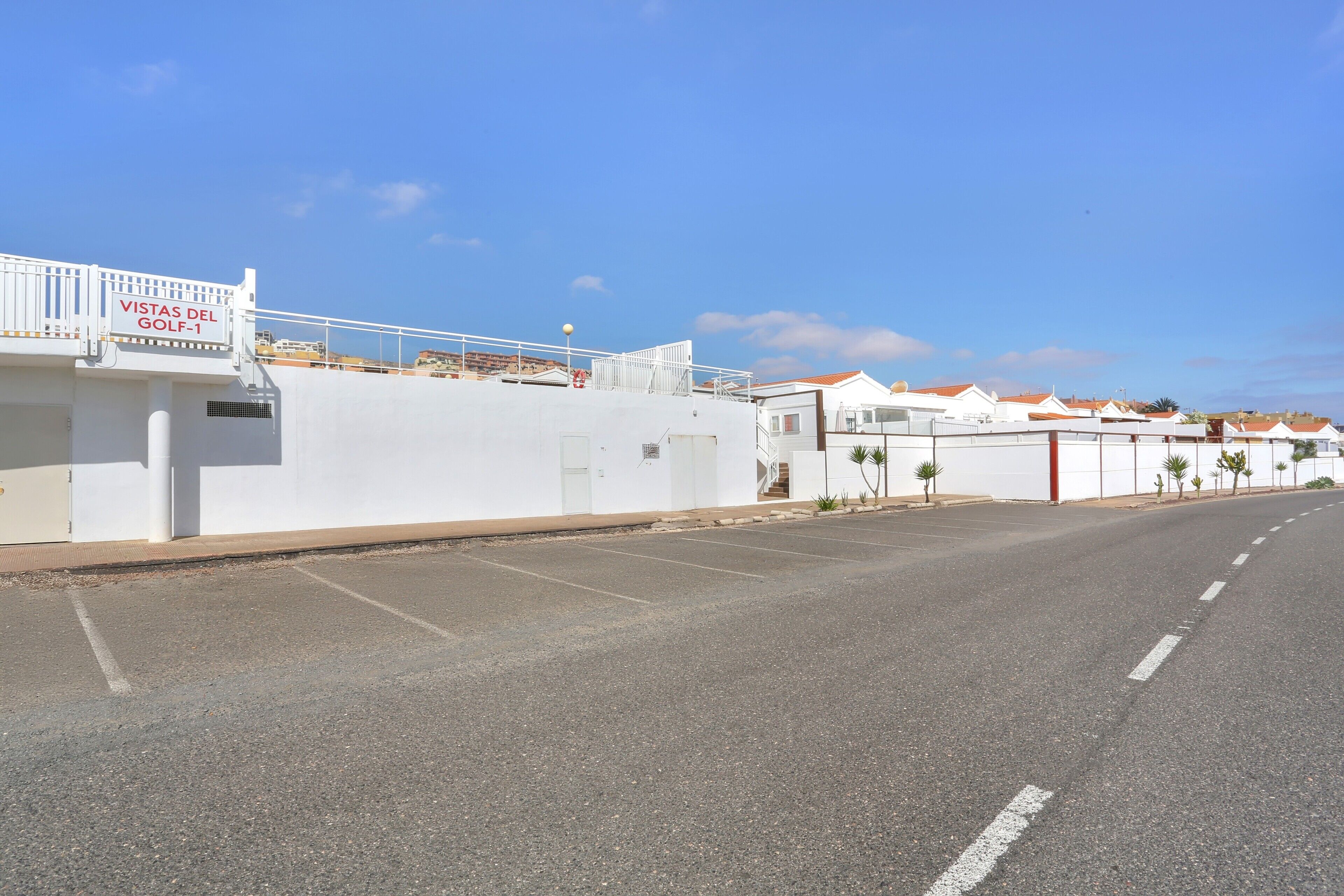 Une vue de rue avec un immeuble portant l’inscription « Vistas del Golf-1 » et un ciel dégagé.