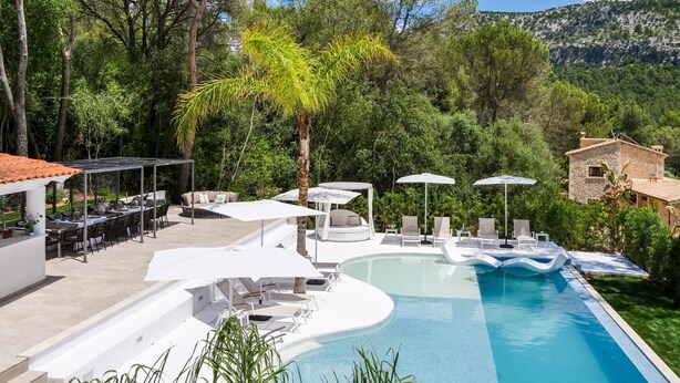 Une piscine entourée de verdure, avec des chaises longues et des parasols, et une chaîne de montagnes en toile de fond.