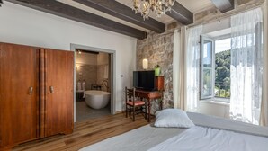 A bedroom with a large bed, a wooden wardrobe, a stone wall, a television, and a bathroom visible through an open door. - Amazing home in Mundanije (Mundanije)