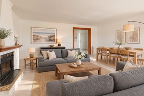 A living room with a fireplace, sofa, coffee table, and dining area with chairs and a table.