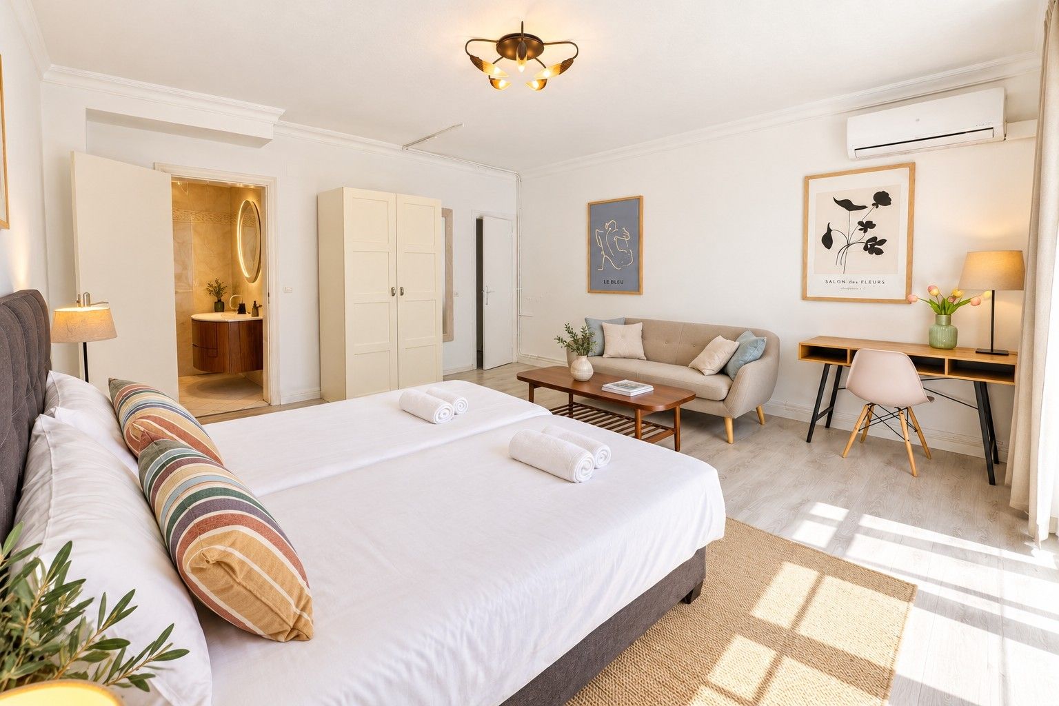 Ein Hotelzimmer mit einem großen Bett, einem Schreibtisch, einer Sitzecke und einem Badezimmer mit Spiegel und Schränken.