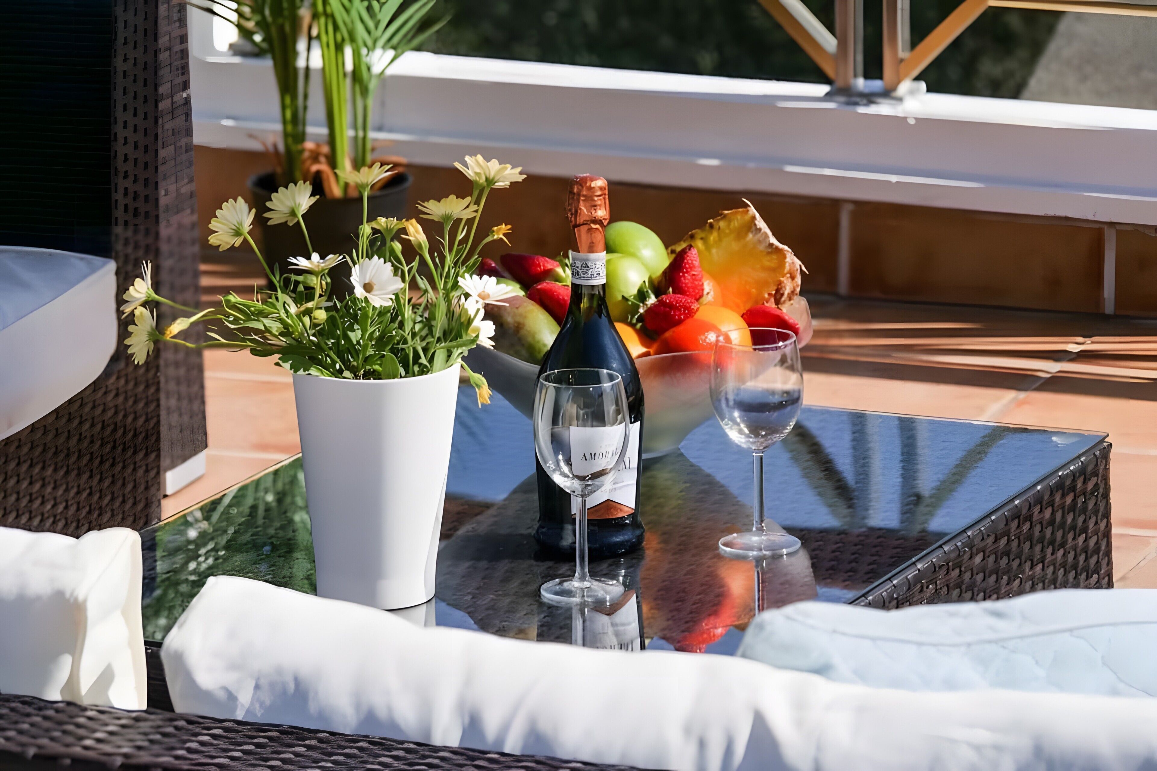 Une table avec une bouteille de champagne, un saladier de fruits et une plante en pot.