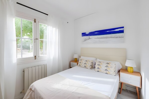 Un dormitorio con una cama, dos mesitas de noche, una ventana y un cuadro colgado en la pared.