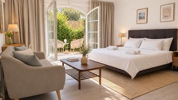 Une chambre d’hôtel avec un lit, un canapé, une table basse et une vue sur un jardin, visible à travers une porte vitrée.