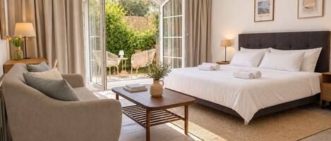 A hotel room with a bed, a sofa, a coffee table, and a view of a garden through a glass door.