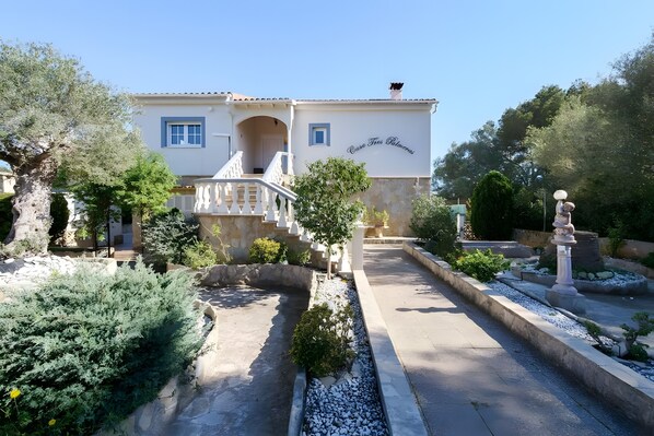 A building with a white facade, a balcony, and a garden with a pathway.