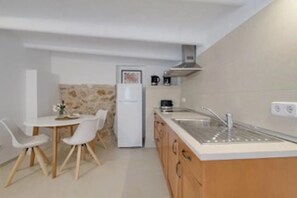 A compact kitchen with a central island, white chairs, a refrigerator, and a coffee machine.