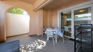 A covered outdoor seating area with a table and chairs, a glass door leading to an interior space, and a view of the outside.