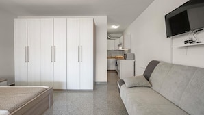 A modern bedroom with a bed, a wardrobe, a kitchenette, and a TV mounted on the wall.