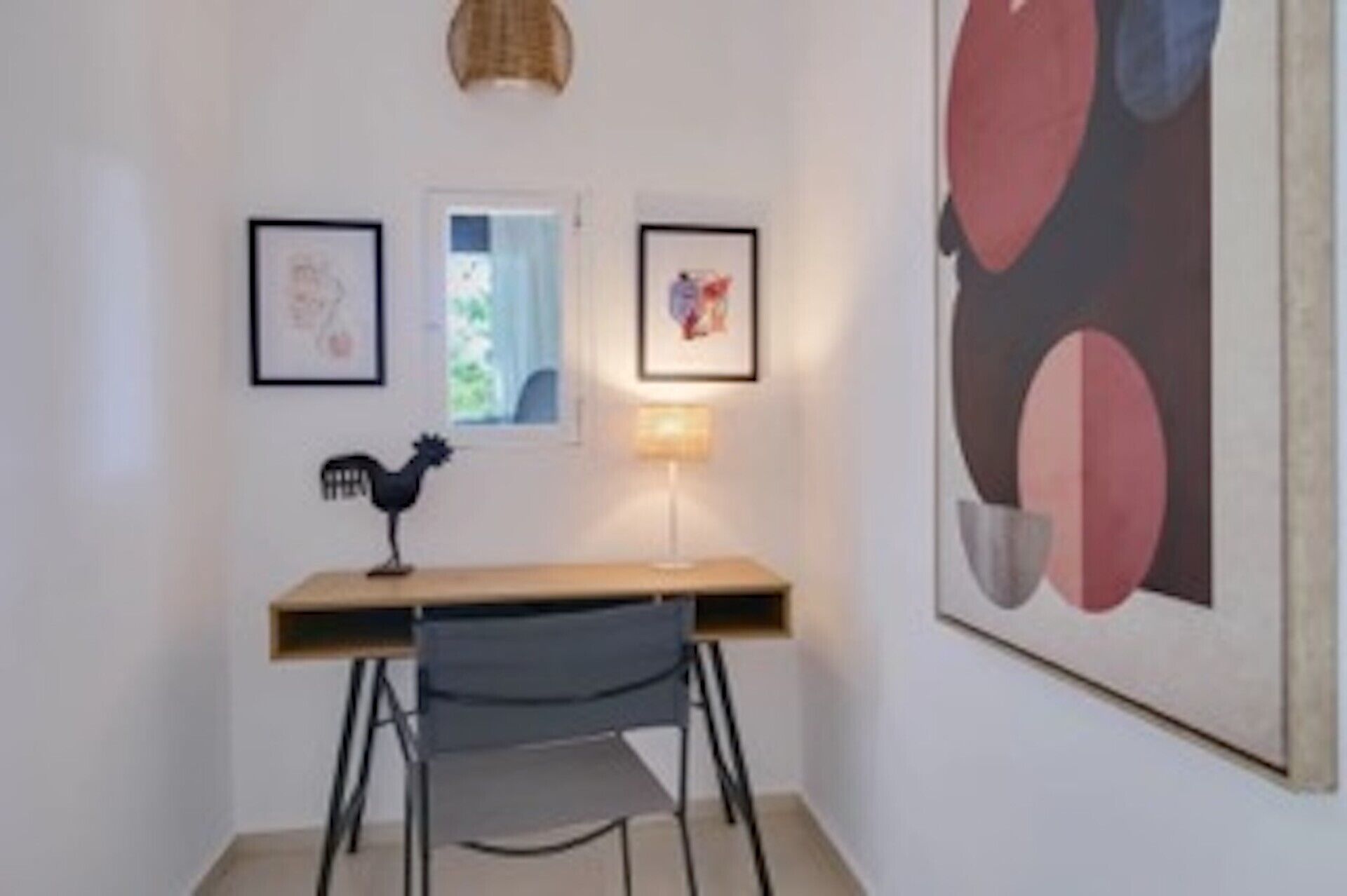 Una habitación con escritorio, silla, una obra de arte enmarcada y una lámpara.