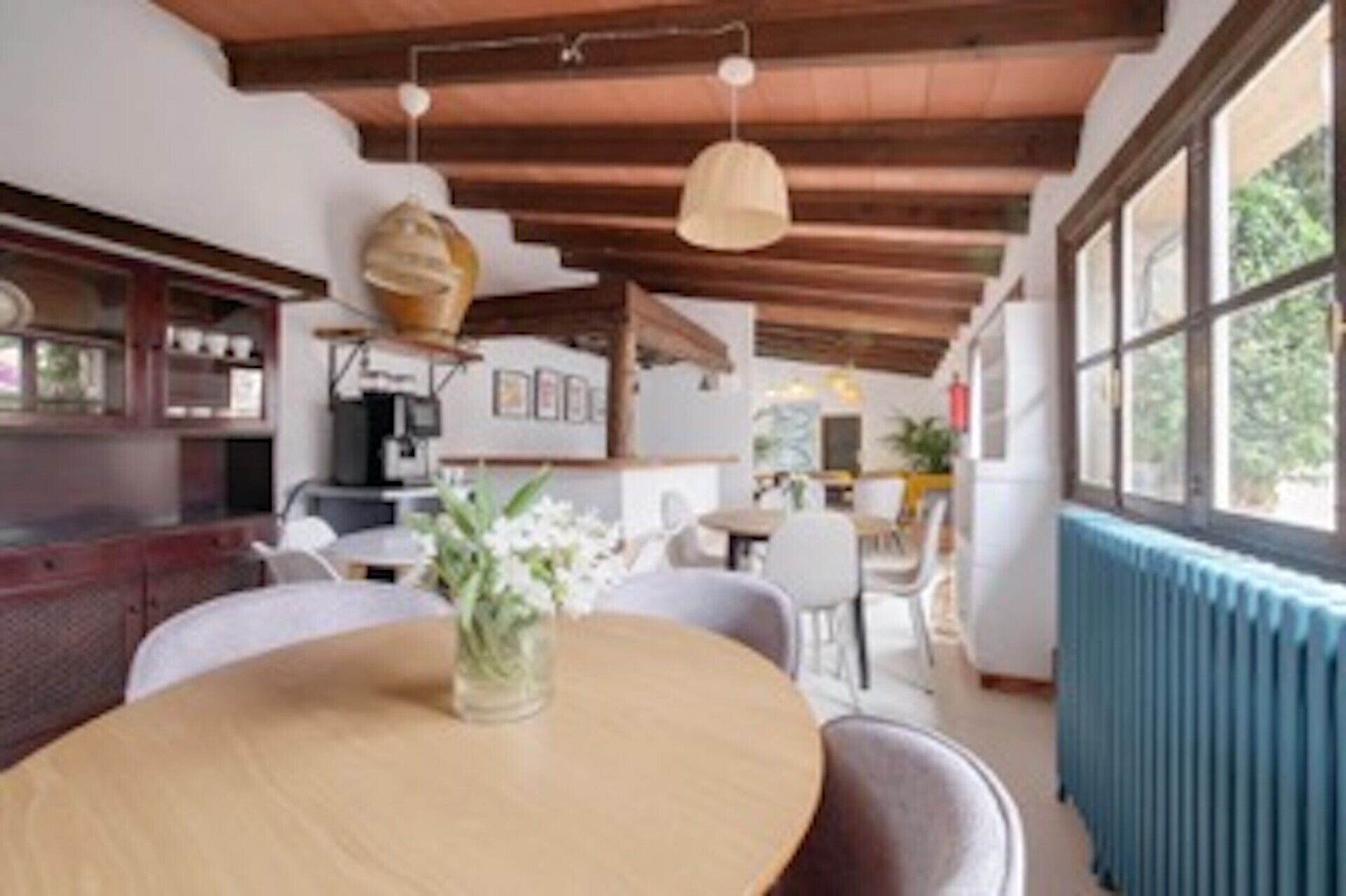 A dining area with a round table, chairs, a vase with flowers, and a ceiling with exposed beams.