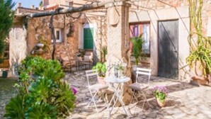 Un patio de piedra con una mesa y sillas, rodeado de plantas en macetas y un rústico muro de piedra.