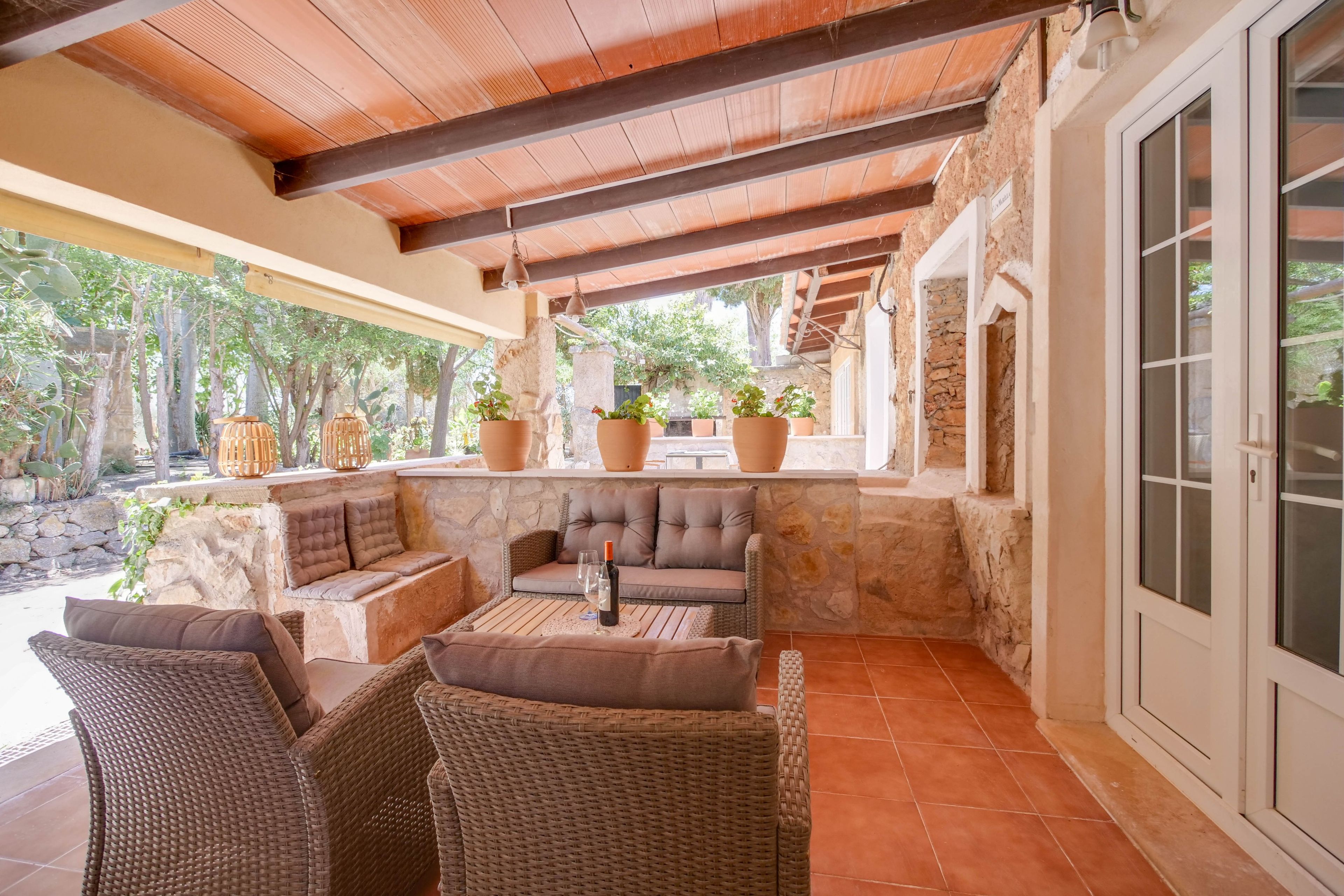 Une terrasse extérieure avec des meubles en osier, des murs en pierre et des plantes en pot.