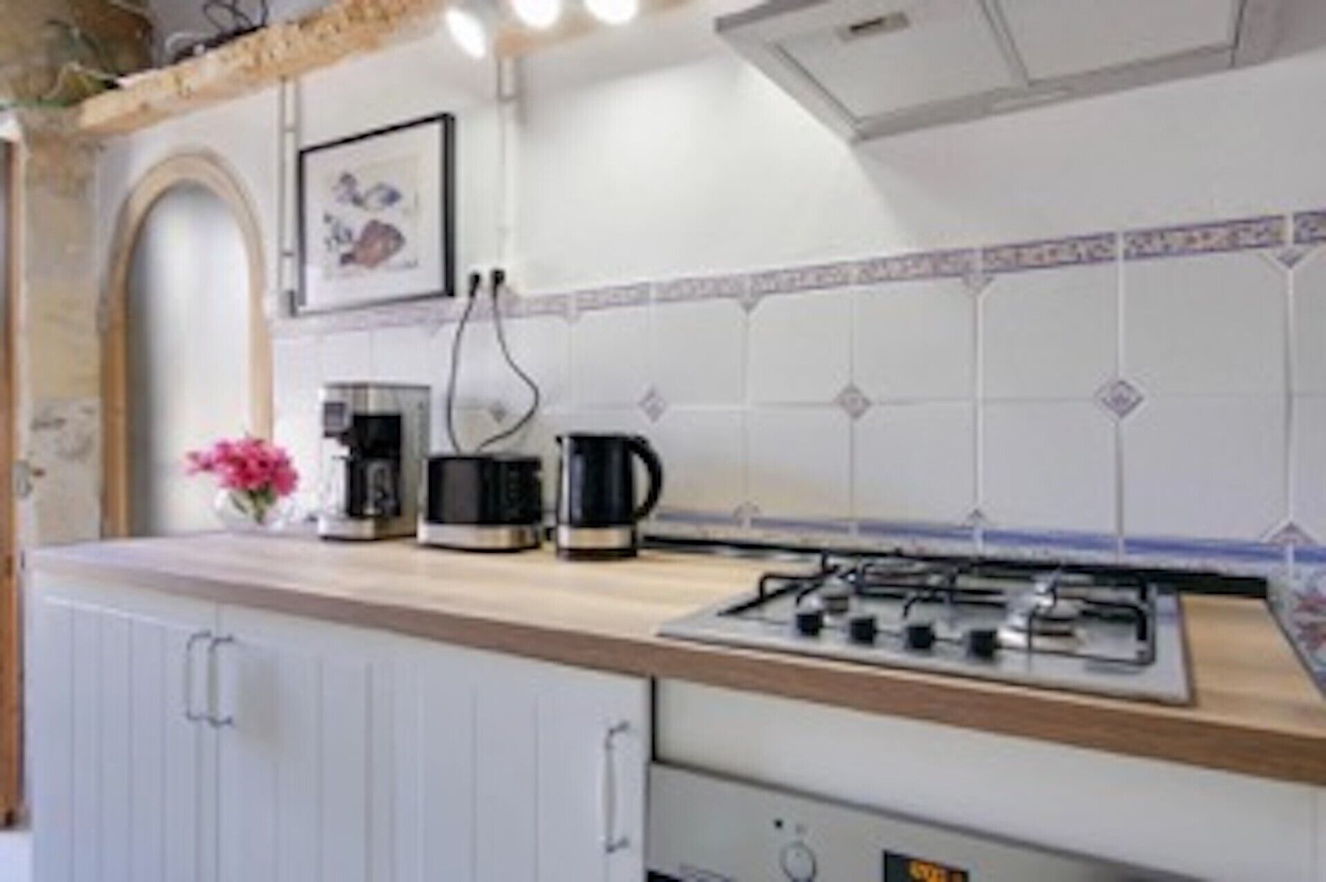 Une cuisine équipée d’une cuisinière à gaz, d’une machine à café et d’une bouilloire posées sur le plan de travail.