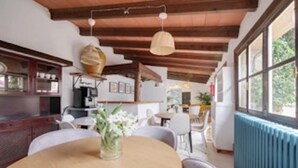 A dining area with a round table, chairs, a vase with flowers, and a ceiling with exposed beams.