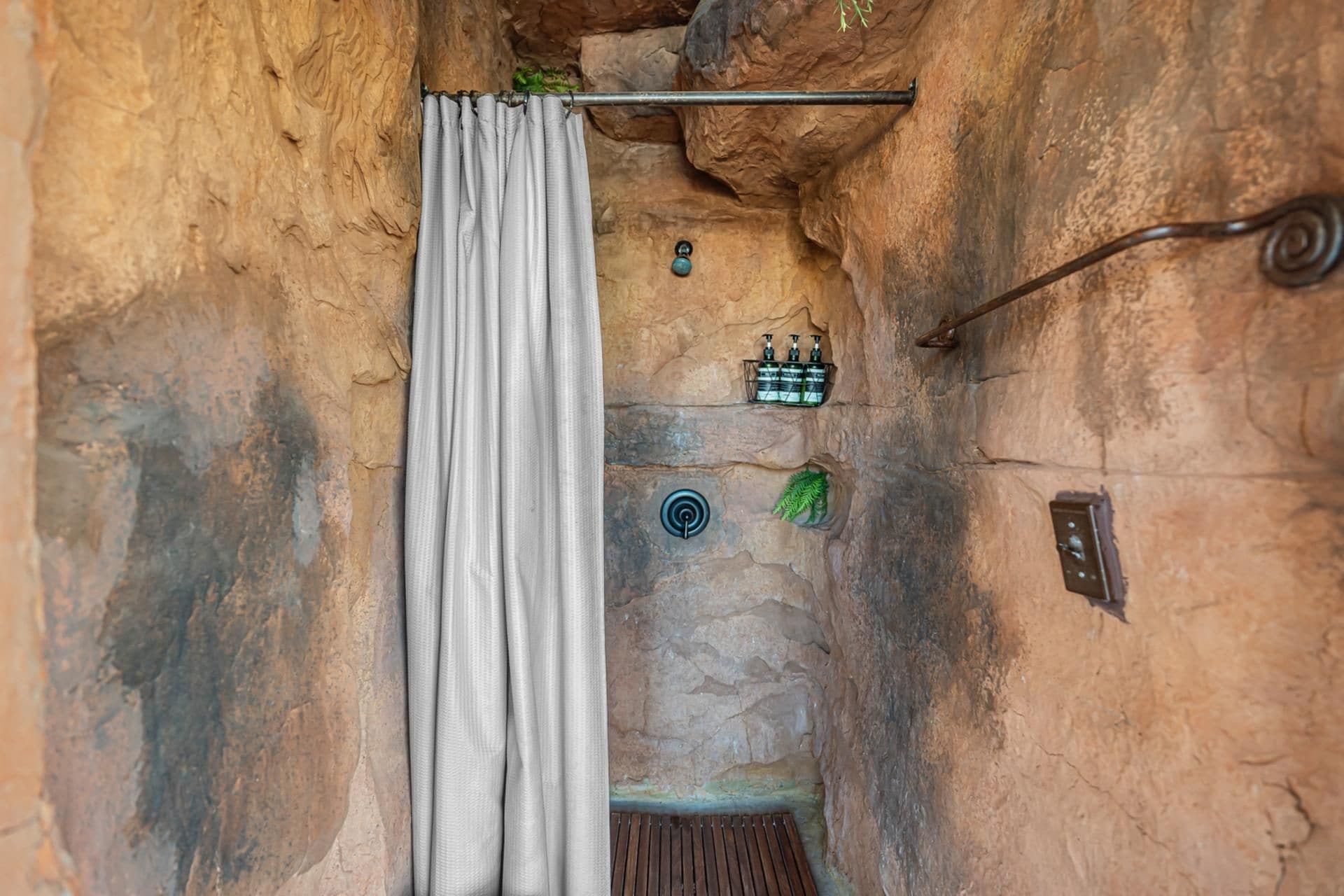 A stone-walled bathroom with a shower curtain, a towel rack, and a small shelf with toiletries.