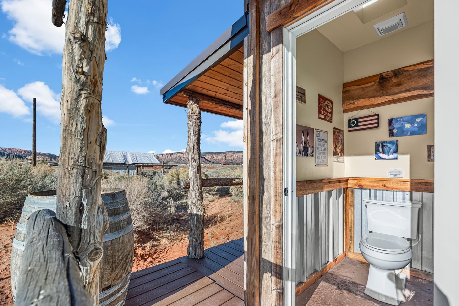 A rustic cabin with a wooden deck, a bathroom with a toilet, and a view of the desert landscape.