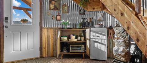 A rustic kitchen with a wooden ceiling, a refrigerator, and a microwave.